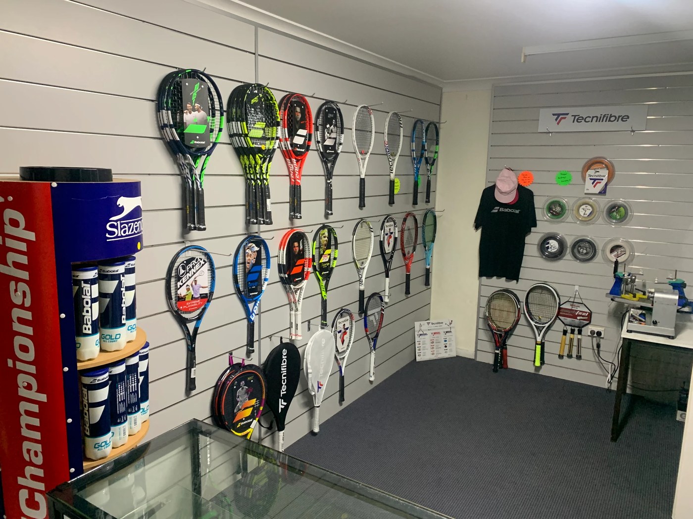 Inside the pro shop: rows of racquets on display, tubes of tennis balls and a restringing machine on the workbench