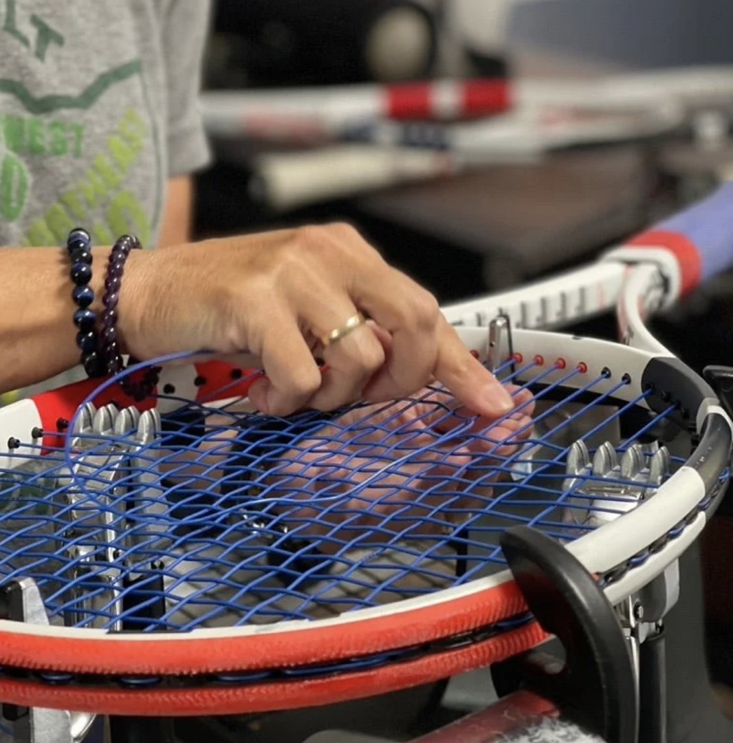 A racquet being restrung on a professional stringing machine, blue strings being woven through the frame
